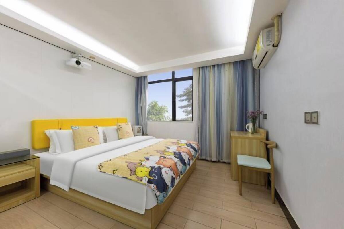 A hotel room with a bed, bedside table, chair, window, and an air conditioning unit.
