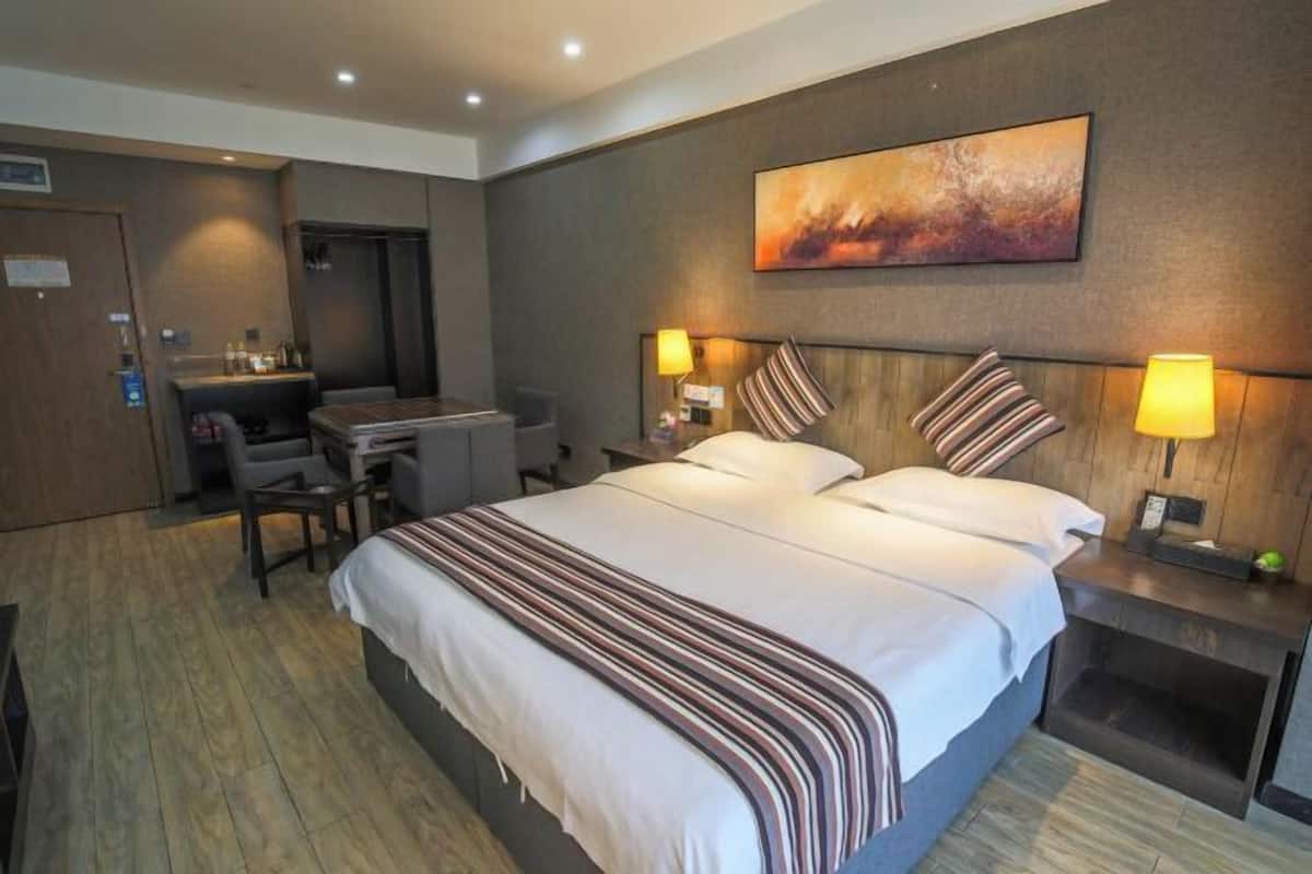 A hotel room with a large bed, two bedside tables with lamps, a desk with a chair, and a painting on the wall.