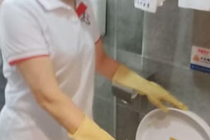 A person in a white uniform with red trim, wearing yellow gloves, handling a white tray.