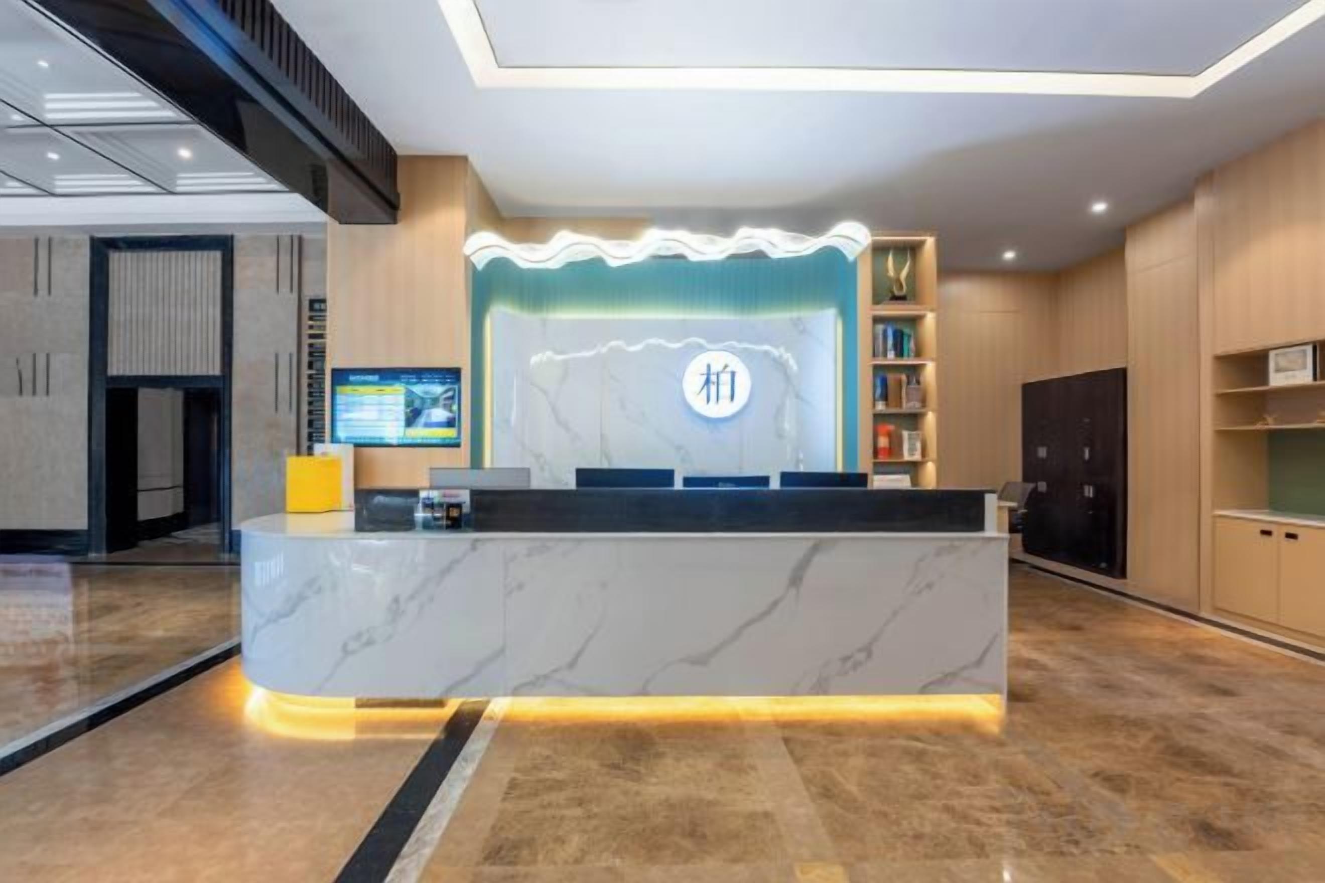 Zona de recepción de hotel con mostrador de mármol, una pantalla digital y un logotipo en la pared.