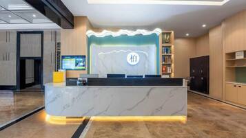 Zona de recepción de hotel con mostrador de mármol, una pantalla digital y un logotipo en la pared.