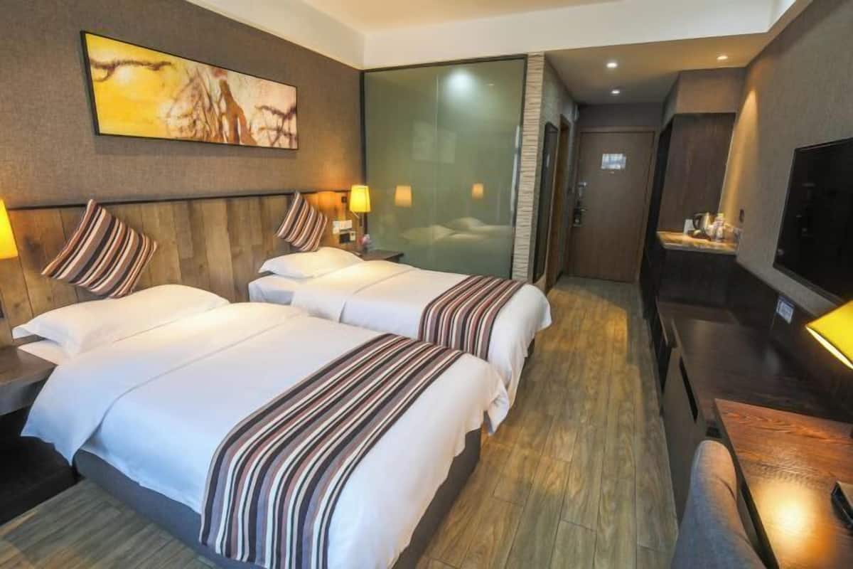 A hotel room with two beds, a TV, a desk, and a painting on the wall.