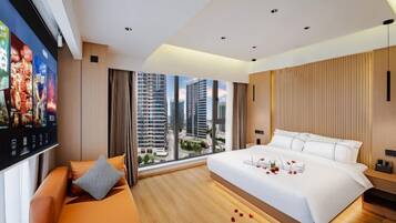 Habitación de hotel moderna con una cama grande, zona de estar, televisión y vistas a la ciudad.