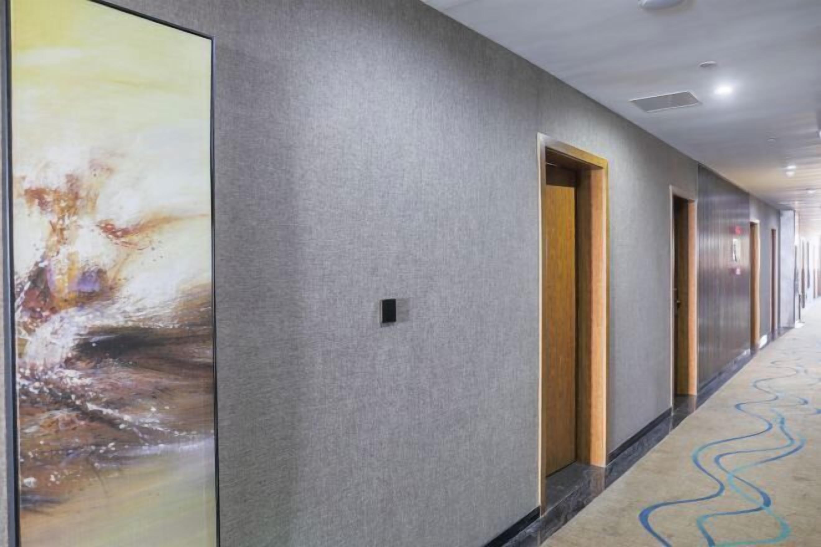 A hallway with a textured gray wall, a large abstract painting, and a wavy carpet pattern.