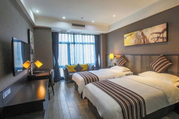 A hotel room with two beds, a desk, a TV, and a large window with curtains.
