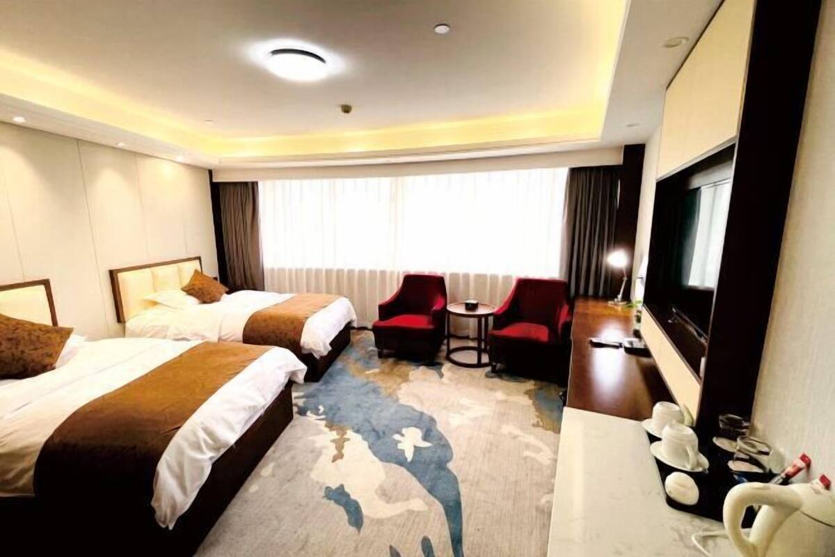 A hotel room with two beds, a TV, a desk with a chair, and a small table.