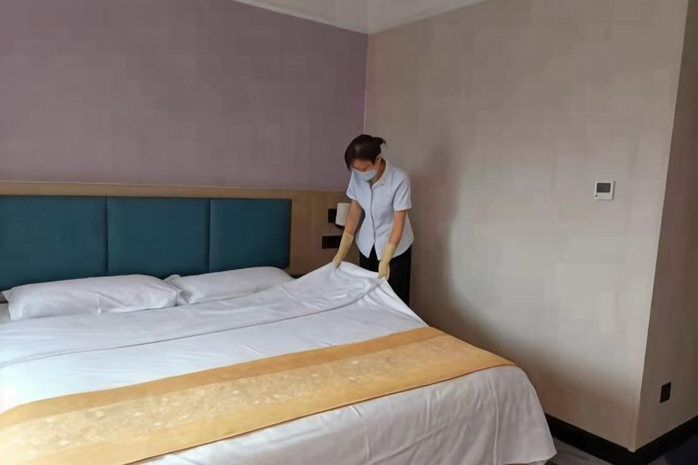 A hotel room with a bed, a headboard, and a wall-mounted light.
