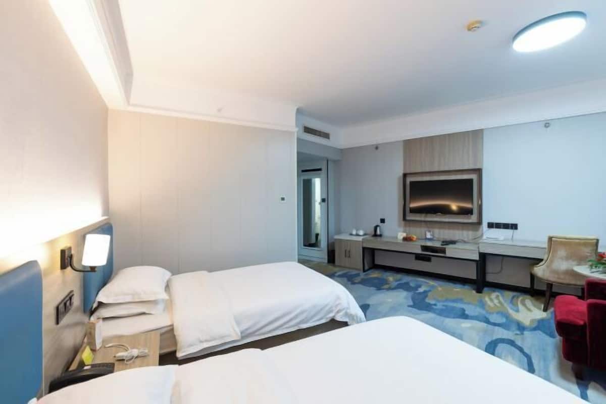 A hotel room with two beds, a desk, a mirror, and a TV.