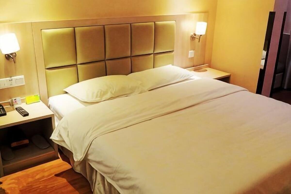 A hotel room with a bed, bedside tables, and wall-mounted lamps.