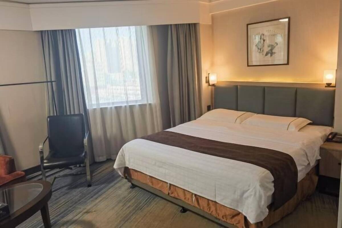 A hotel room with a bed, a chair, a desk, and a window with curtains.