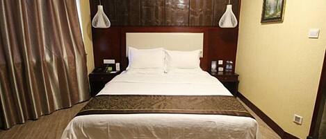 Habitación de hotel con una cama grande, dos mesitas de noche, una mesita auxiliar, cabecero y un cuadro en la pared, además de una cortina.