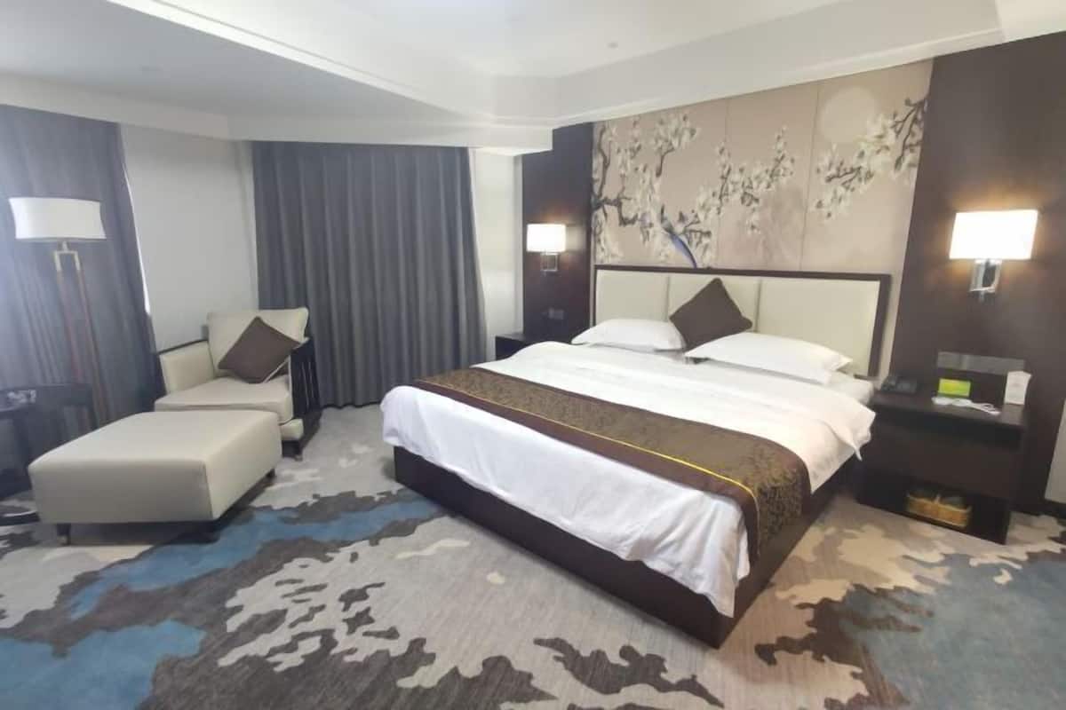 A hotel room with a large bed, a sofa, a desk, and a lamp.