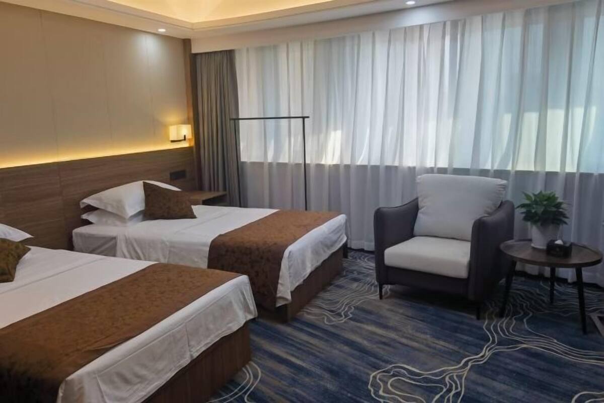 A hotel room with two beds, a sofa, a small table, and a floor lamp.
