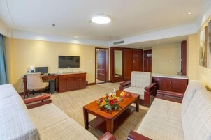 Habitación de hotel con sofá, una mesita con un centro de mesa floral, televisor, escritorio con computadora y armario.