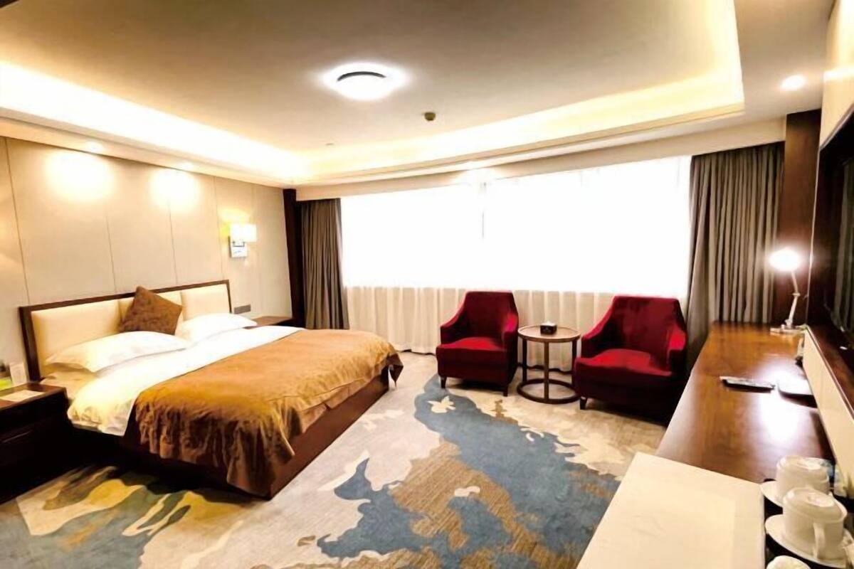 A hotel room with a large bed, two red armchairs, a small table, and a TV.