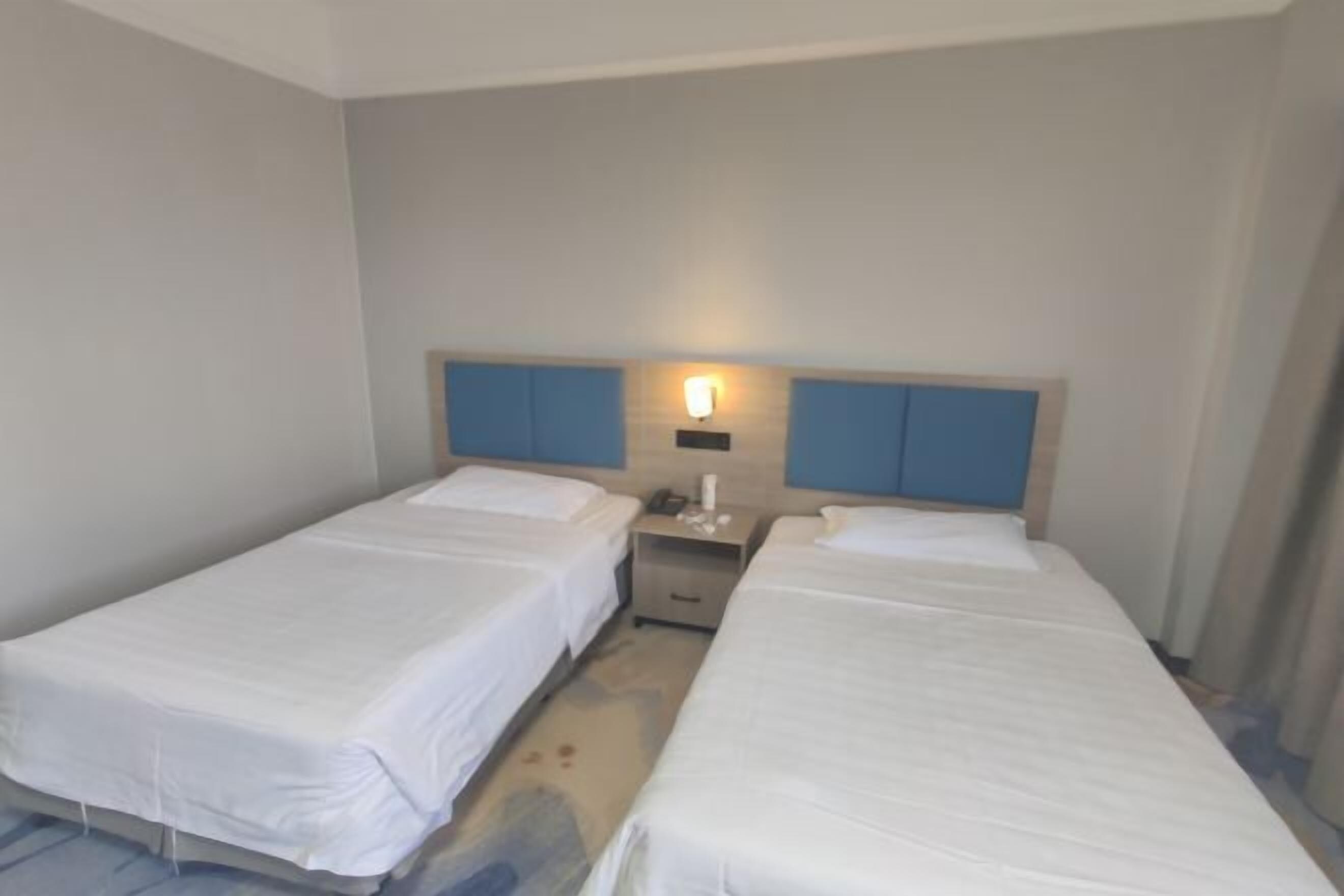 Una habitación de hotel con dos camas individuales, una mesita de noche con lámpara y una lámpara de pared.