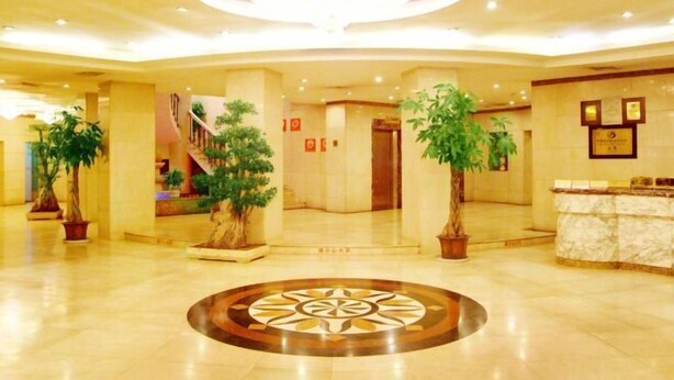 A spacious lobby with a central circular floor design, potted plants, a reception desk, and a staircase leading to upper floors. - Railway Grand Hotel (Xiangyang)