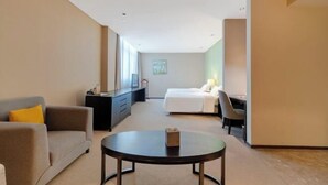 A hotel room with a sofa, a bed, a desk, and a small table. - Gallery Hotel (Zhangjiagang)