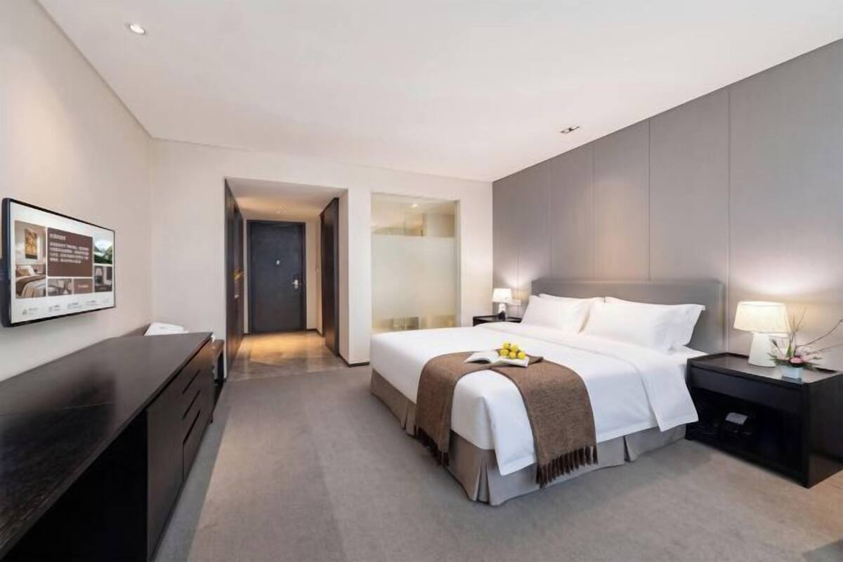 Moderni hotellihuone, jossa on suuri sänky, yöpöydät, työpöytä ja seinällä oleva taulu.
