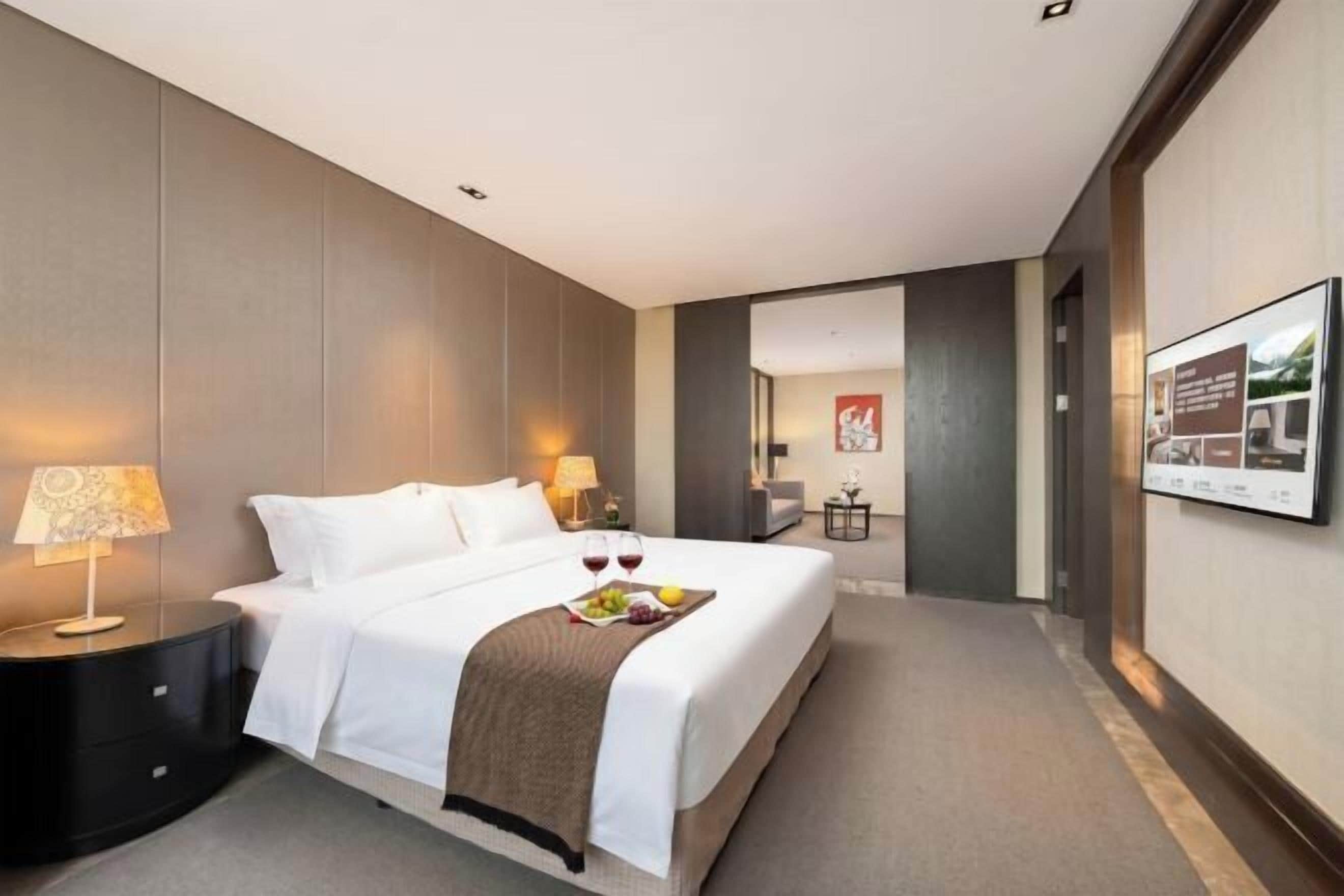 A hotel room with a bed, bedside tables, a lamp, a fruit basket, and a framed picture on the wall.