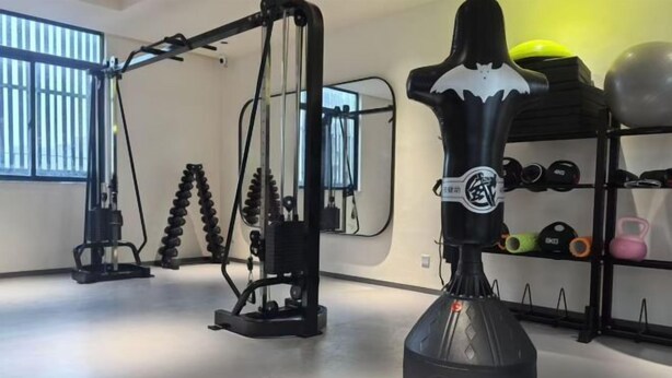 A gym with exercise equipment, including a cable machine, a squat rack, and a punching bag. - Gallery Hotel (Zhangjiagang)