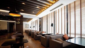 A modern lounge area with sofas and tables, large windows with blinds, and a wooden ceiling with integrated lighting. - Gallery Hotel (Zhangjiagang)