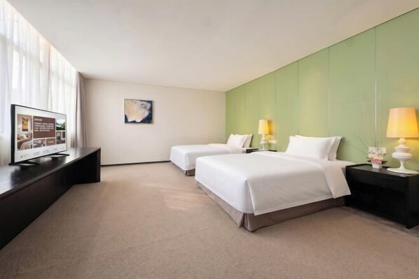A hotel room with two beds, a flat-screen TV, a green accent wall, and a nightstand with a lamp. - Gallery Hotel (Zhangjiagang)