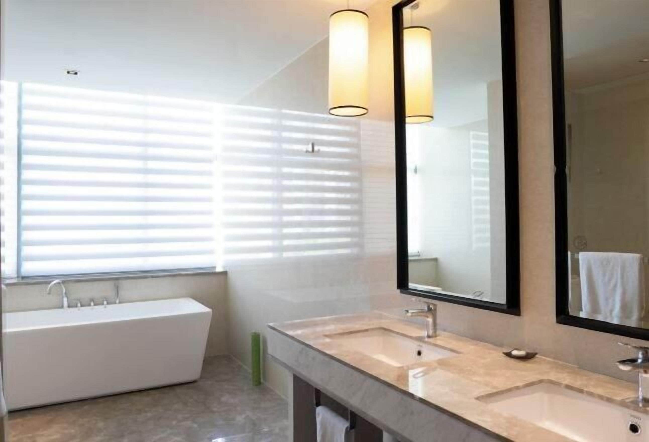 A modern bathroom with a bathtub, two sinks, and a large mirror.