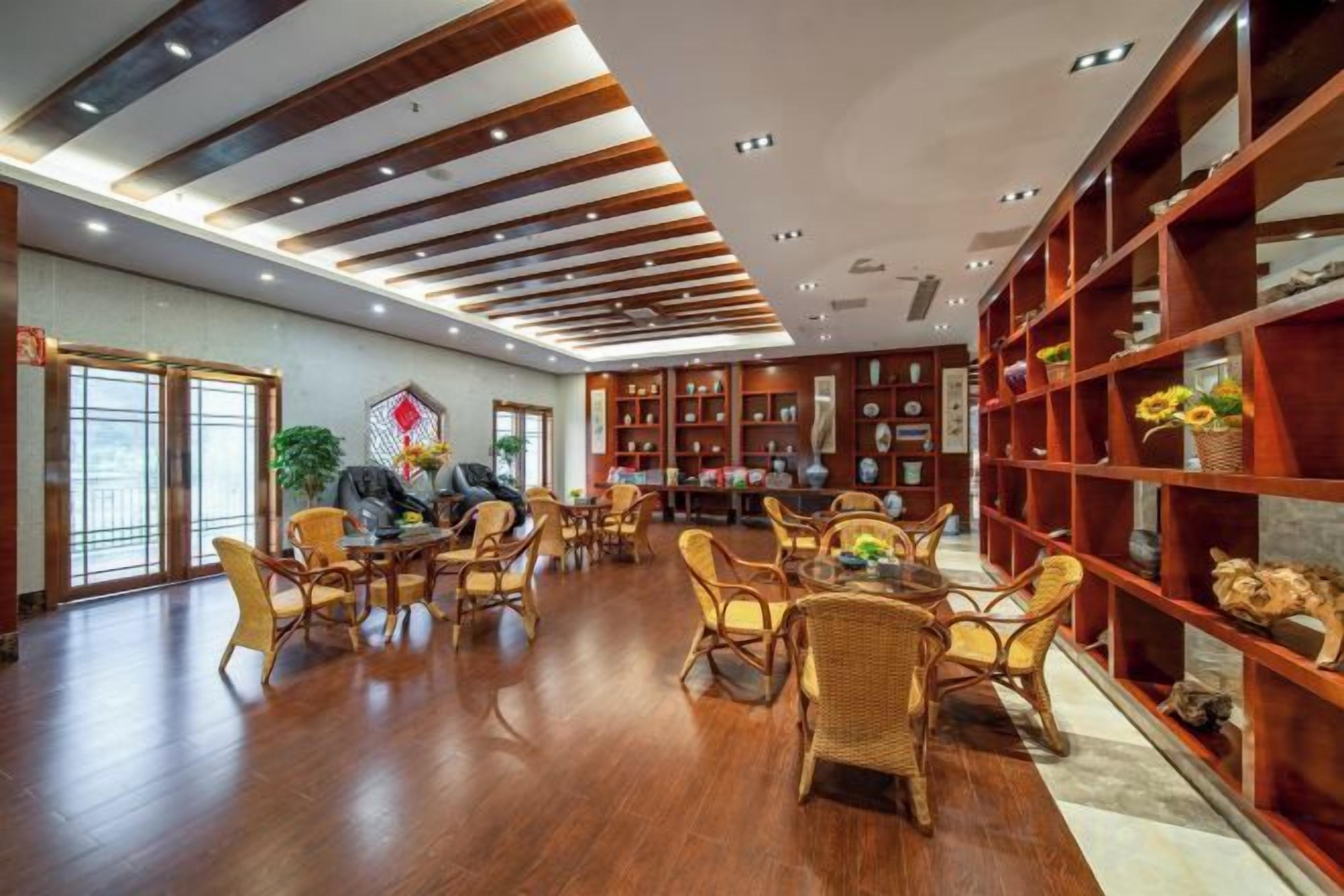A spacious room with a high ceiling, wooden flooring, and a central seating area with chairs and tables.