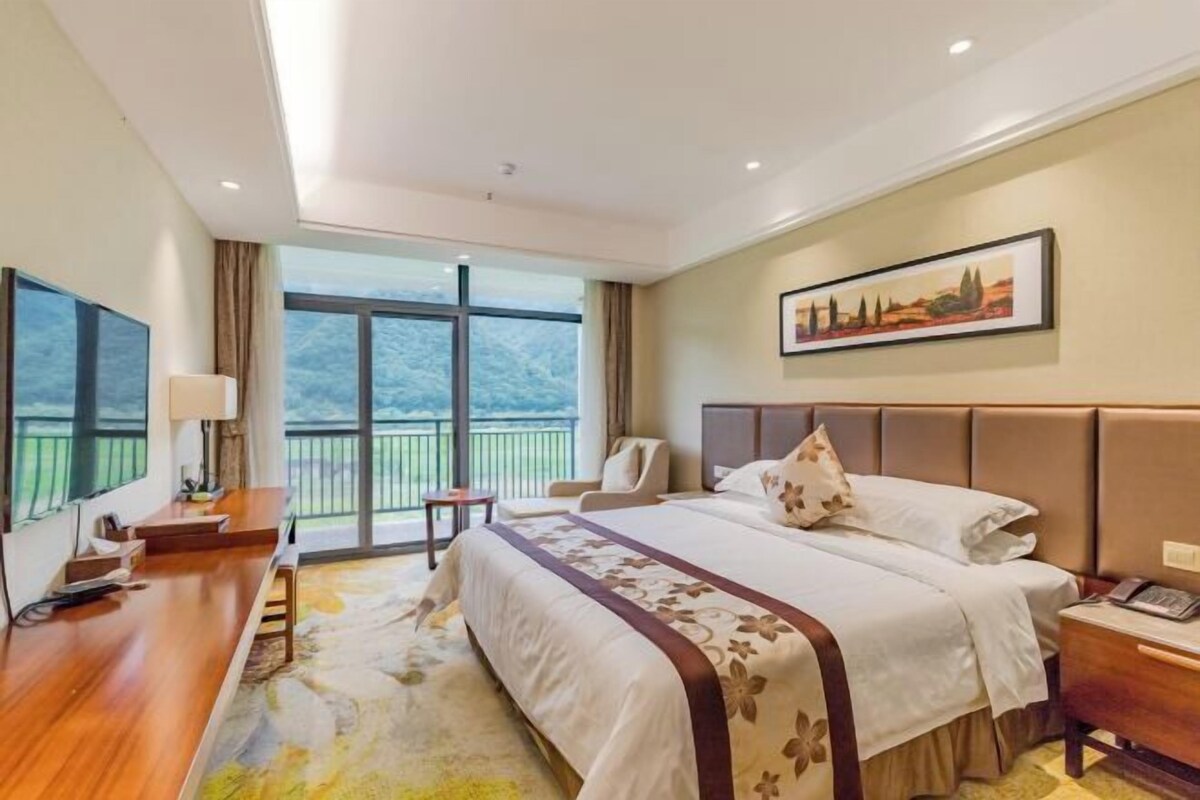 A hotel room with a large bed, a desk, a chair, a TV, and a painting on the wall.