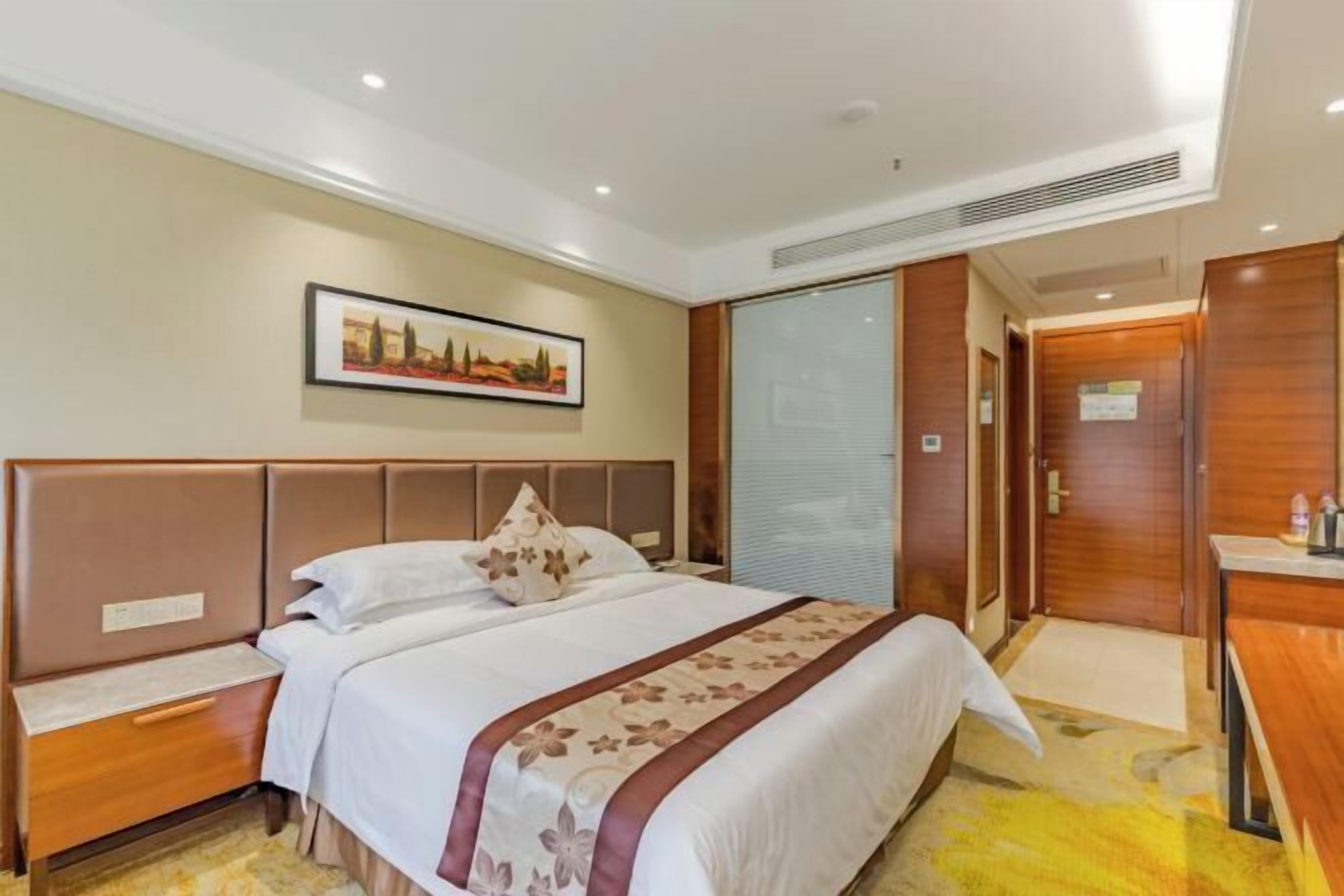 Una habitación de hotel con una cama grande, una mesita de noche, un escritorio y un cuadro en la pared.