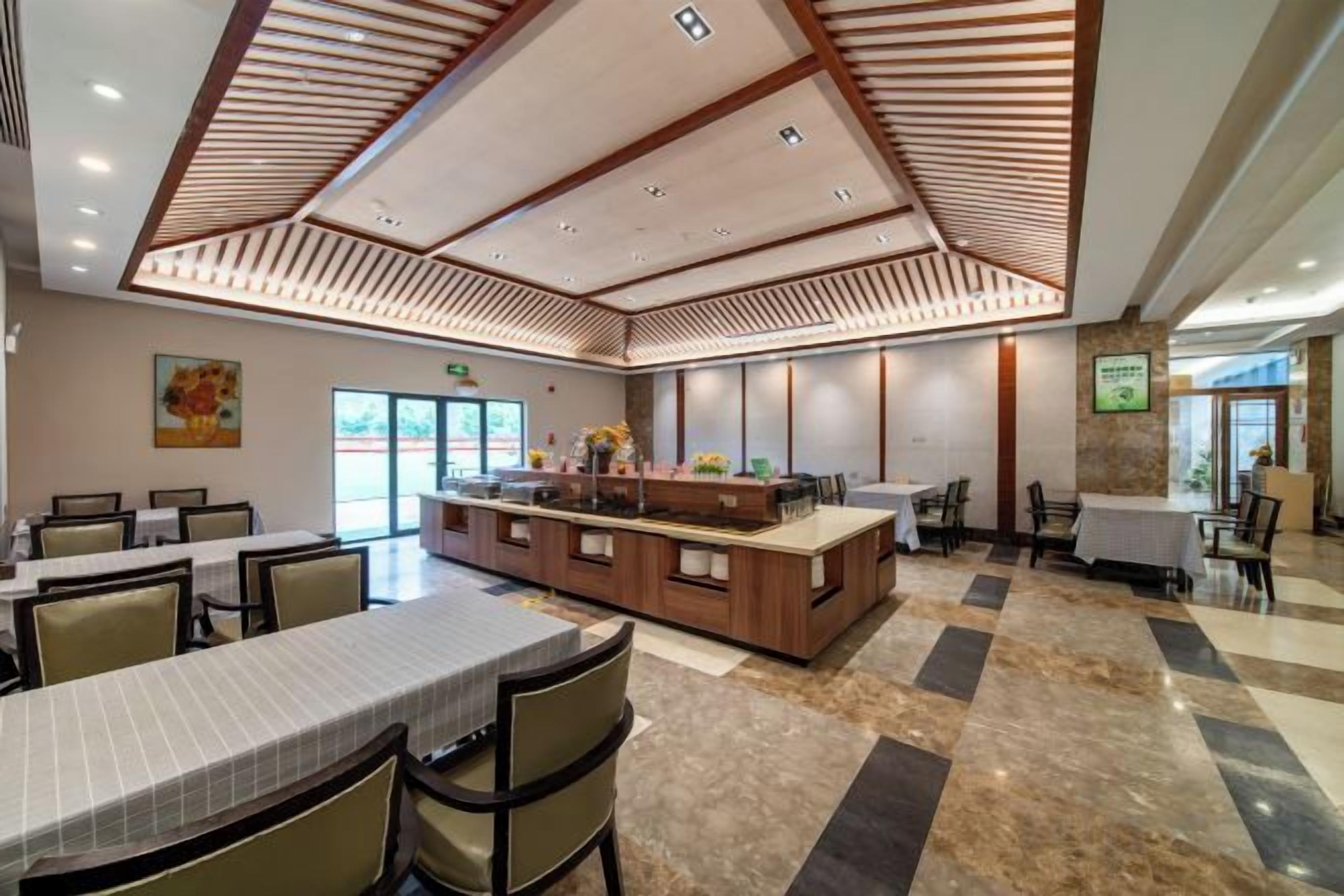 Un comedor de hotel amplio con varias mesas y sillas, una isla central con mostrador y un techo alto con listones de madera.