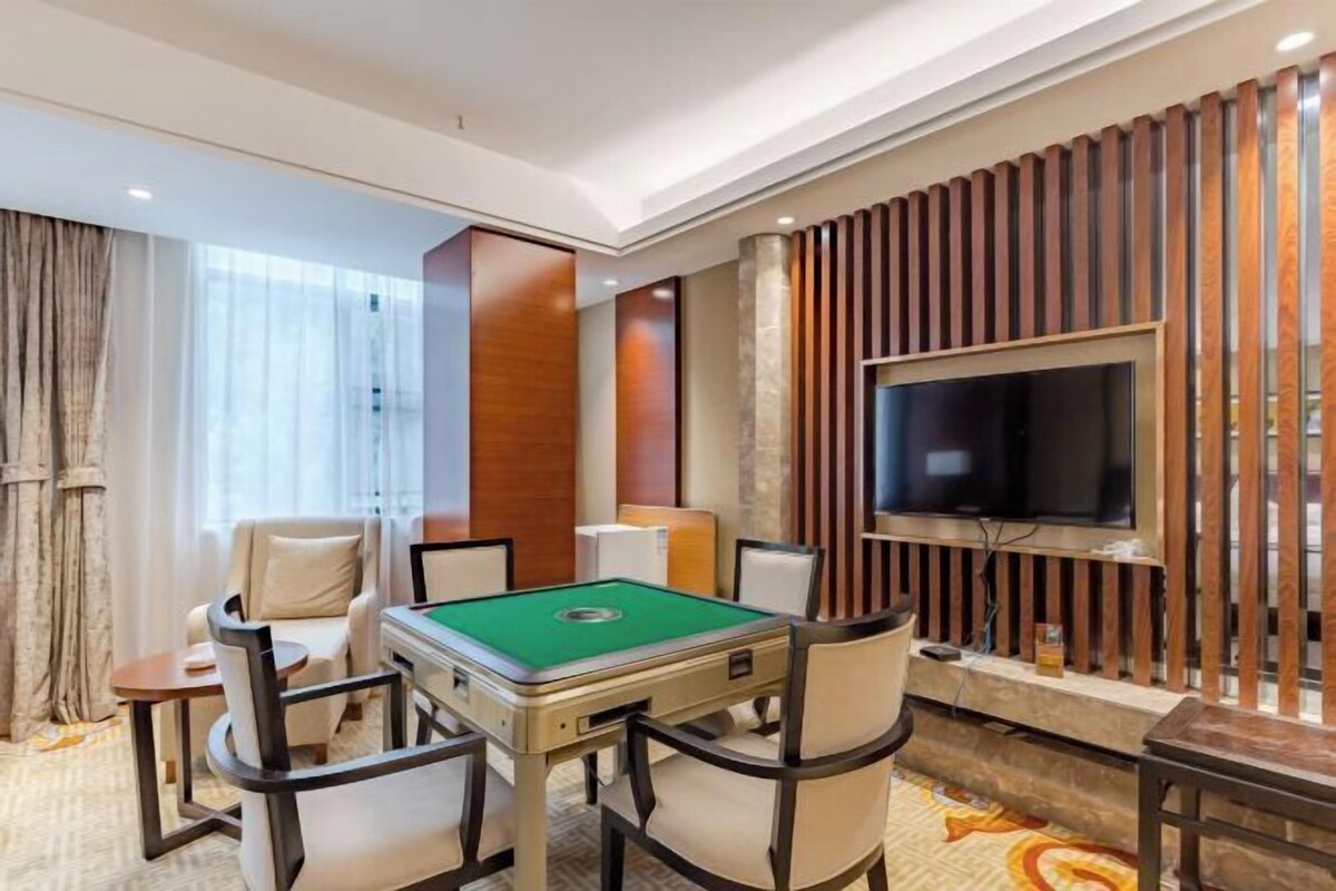 A hotel room with a pool table, comfortable seating, a flat-screen TV, and a decorative wall panel.