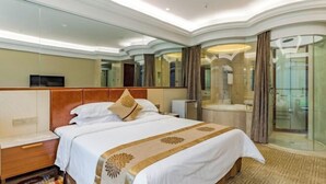 Habitación de hotel con una cama grande, una mesita de noche, un espejo y un baño con cabina de ducha de vidrio.