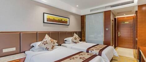 A hotel room with two beds, a wooden headboard, a painting on the wall, and a door with a wooden panel.