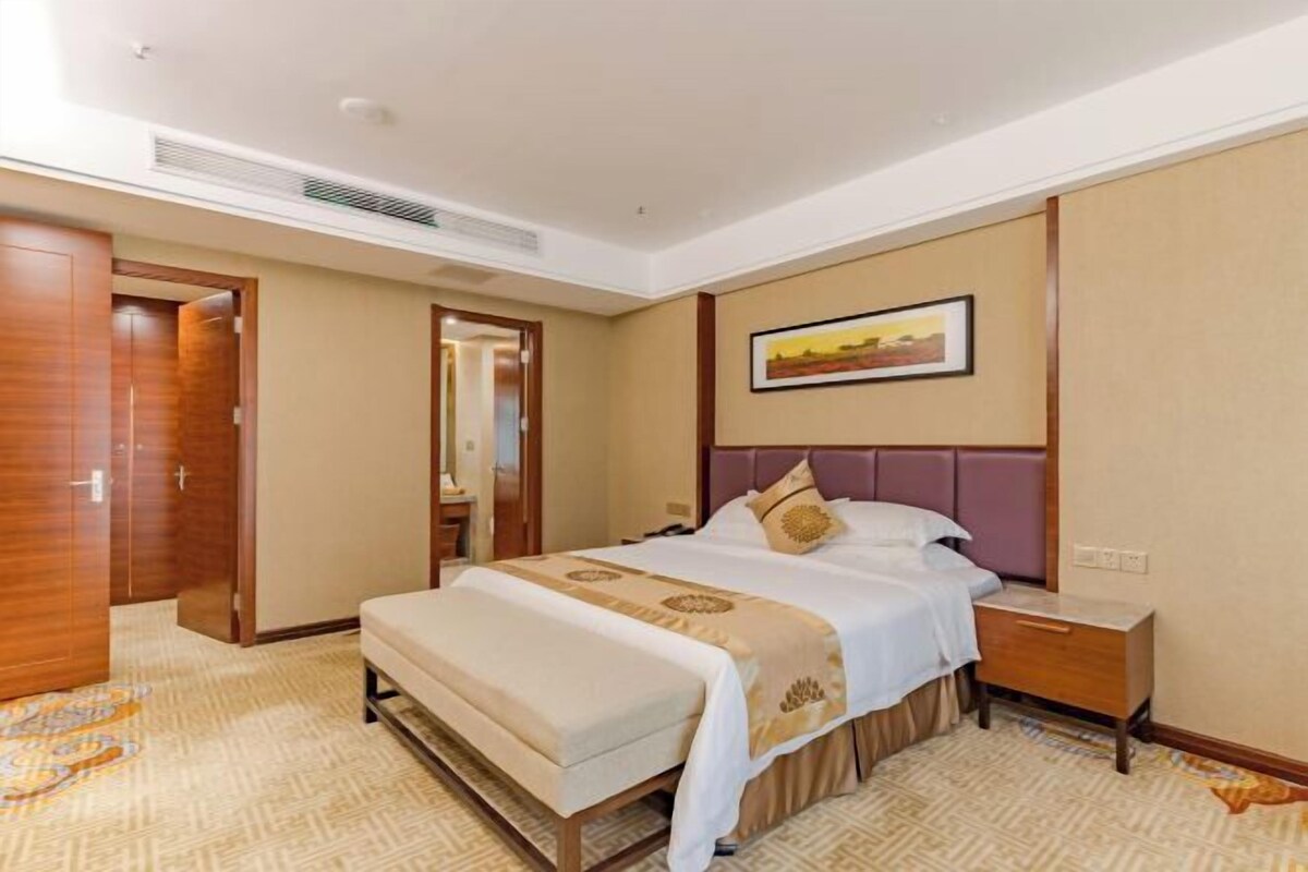 A hotel room with a bed, bedside table, and a painting on the wall.