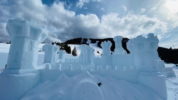 Une sculpture de château en neige, avec un fossé et des tours.