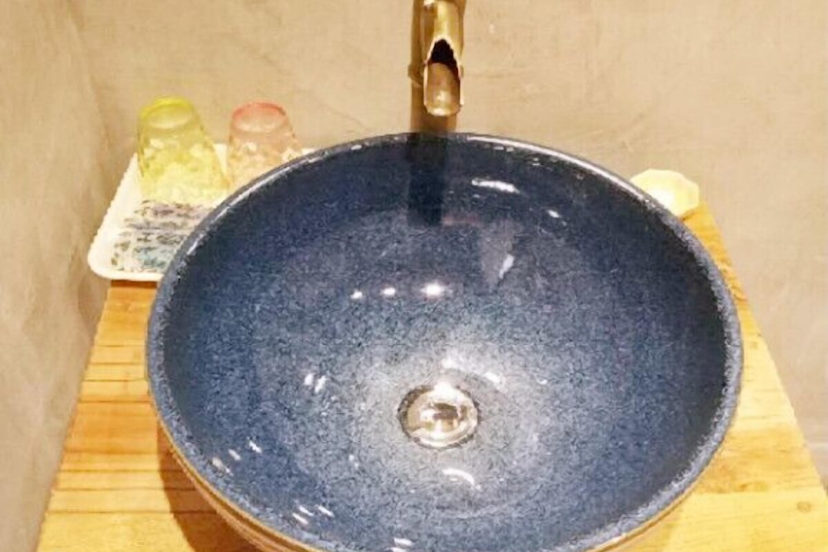 Een ronde, donkerblauwe keramische wasbak met een messing kraan op een houten oppervlak.