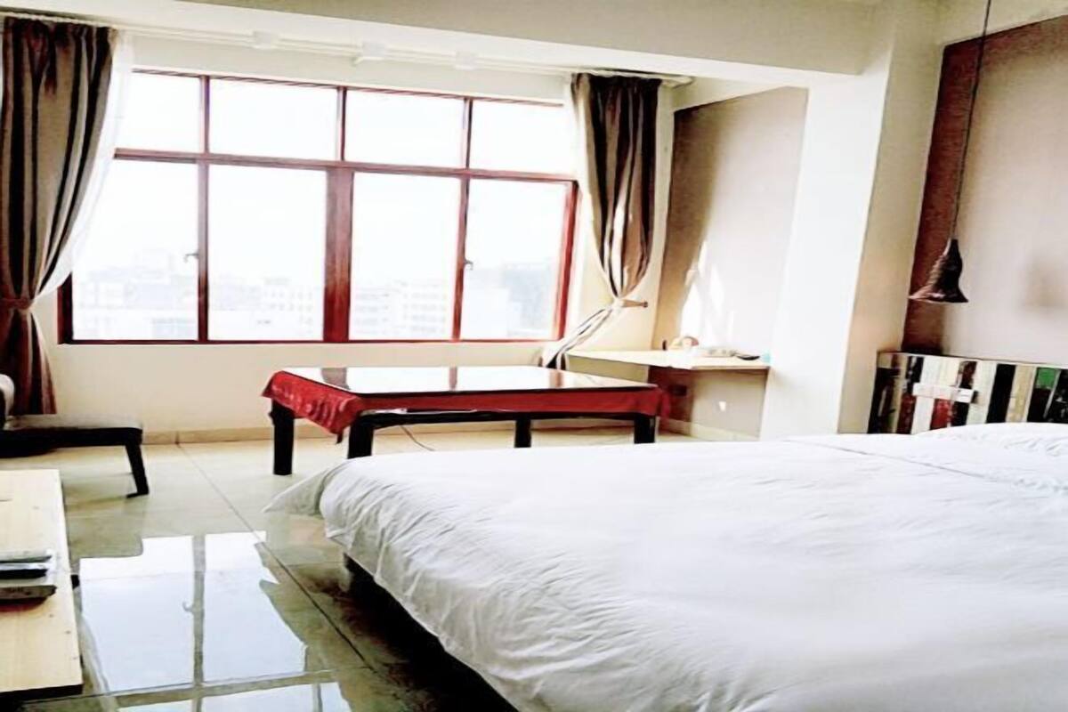 A hotel room with a bed, a desk, a chair, a window with curtains, and a bedside table.