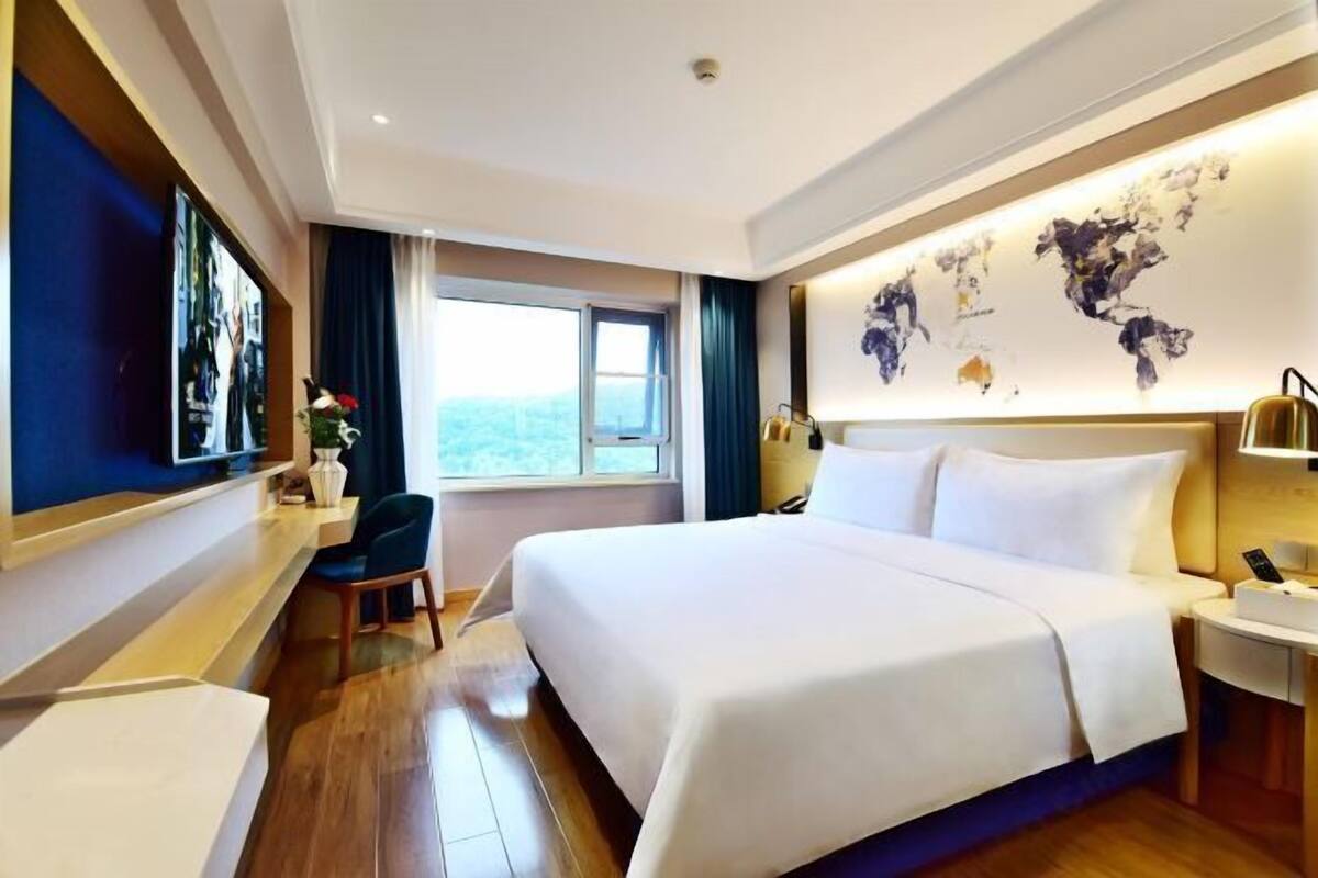 A hotel room with a large bed, a desk, a chair, a window with a view, and a world map on the wall.