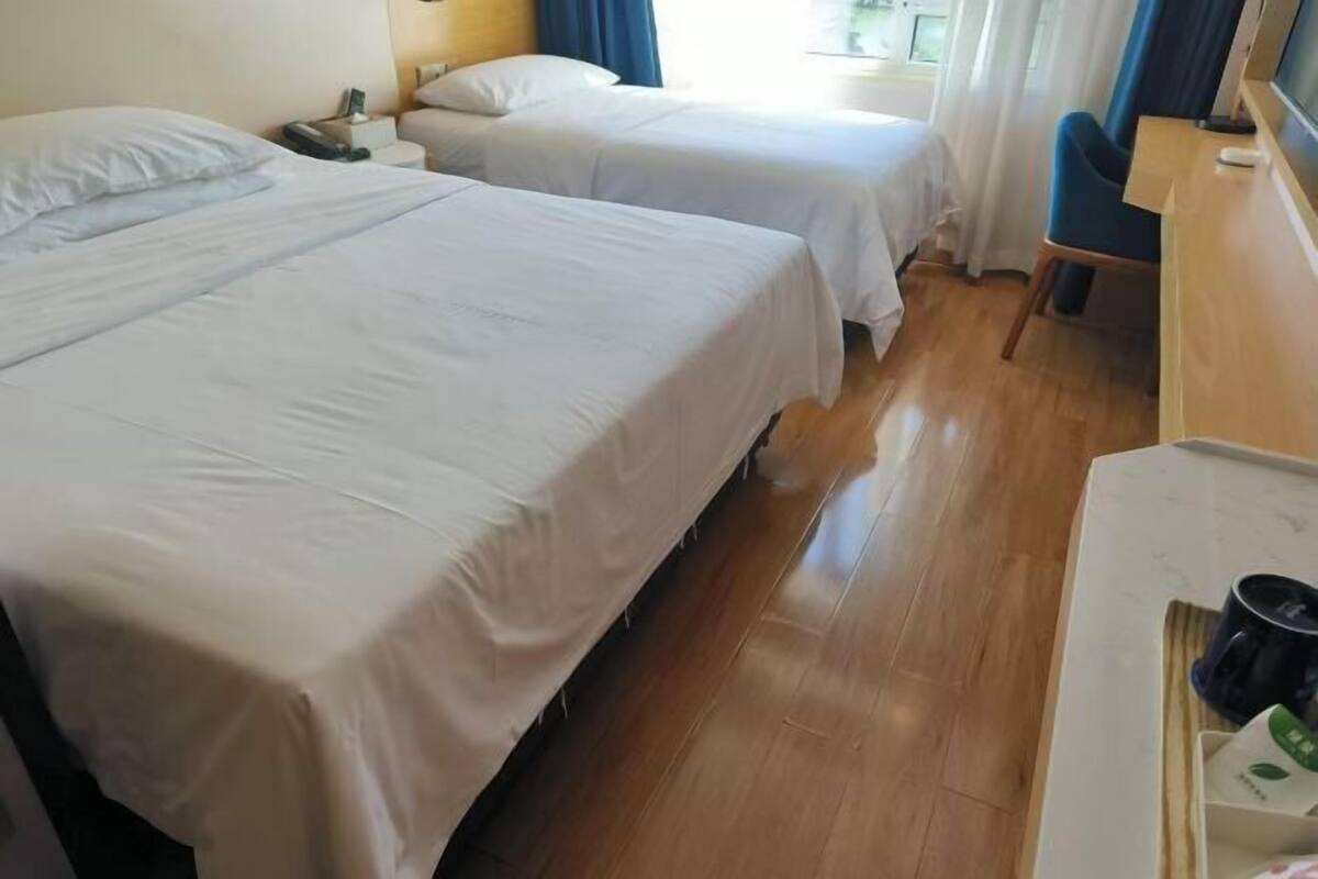 A hotel room with two beds, a wooden desk, and a chair.