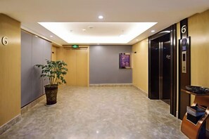 A hotel lobby with a marble floor, a potted plant, an elevator, and a reception desk. - Wanhou Academy of Fine Arts Hotel (Yiyang Xiufeng Park Branch) (Yiyang)