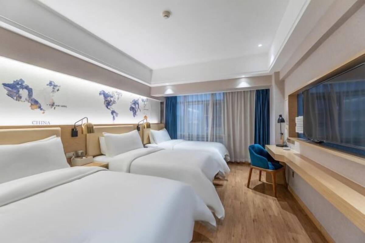 A hotel room with two beds, a desk, a chair, and a large window with curtains.