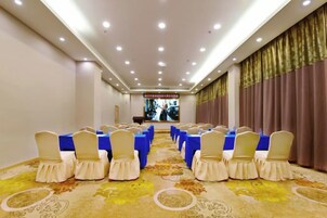 Un salón de conferencias con filas de sillas y mesas, piso alfombrado y un amplio ventanal con cortinas.