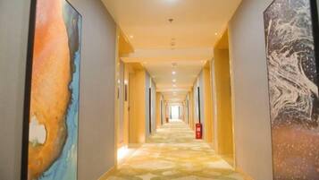 A hotel hallway with a patterned carpet, framed artwork on the walls, and a fire extinguisher.