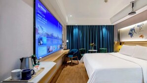 A hotel room with a bed, a desk with a computer, a coffee maker, and a TV displaying a welcome screen. - Wanhou Academy of Fine Arts Hotel (Yiyang Xiufeng Park Branch) (Yiyang)