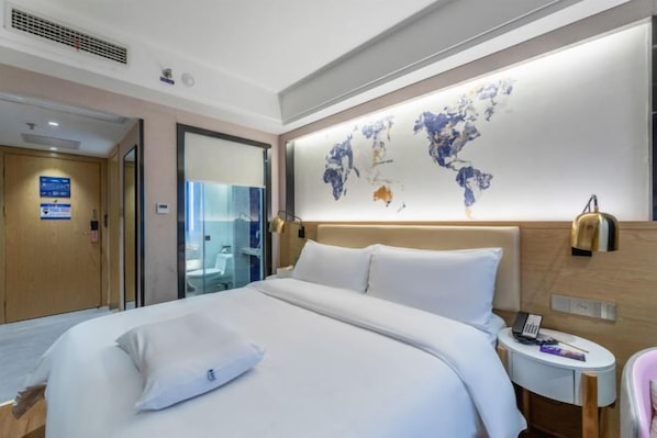 Una habitación de hotel moderna con una cama grande, una mesita de noche con lámpara, un mapa del mundo en la pared y un baño visible a través de una puerta de cristal.