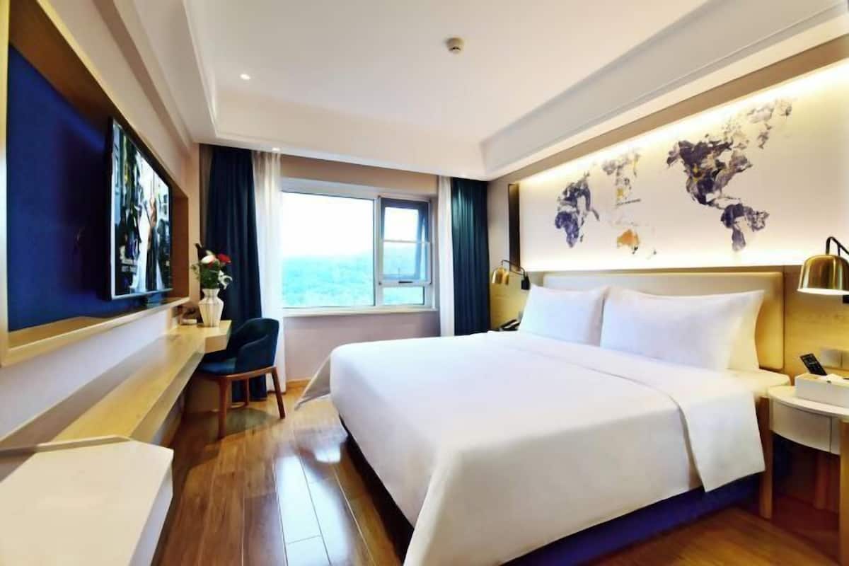 A hotel room with a large bed, a desk, a chair, a window, and a world map on the wall.