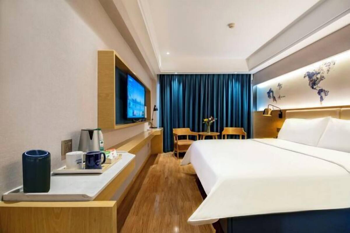 A hotel room with a bed, a desk with a coffee maker, a TV, and a seating area with chairs and a table.