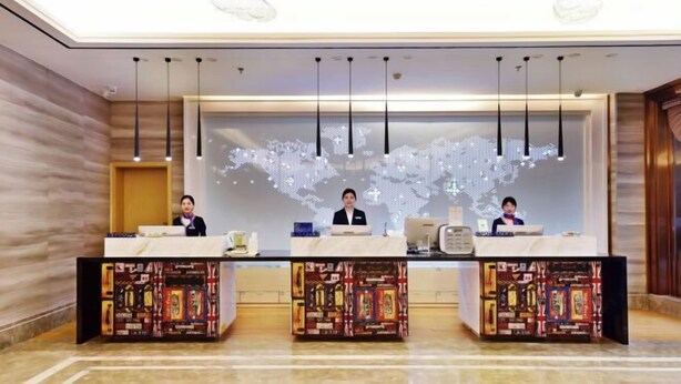 A hotel reception area with three receptionists, a digital world map display, and patterned reception desks. - Wanhou Academy of Fine Arts Hotel (Yiyang Xiufeng Park Branch) (Yiyang)